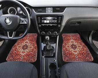 May include: Car interior with two floor mats. The mats have a red, beige, and brown oriental rug design. The car's dashboard is gray, and the seats are dark gray. The steering wheel is black.
