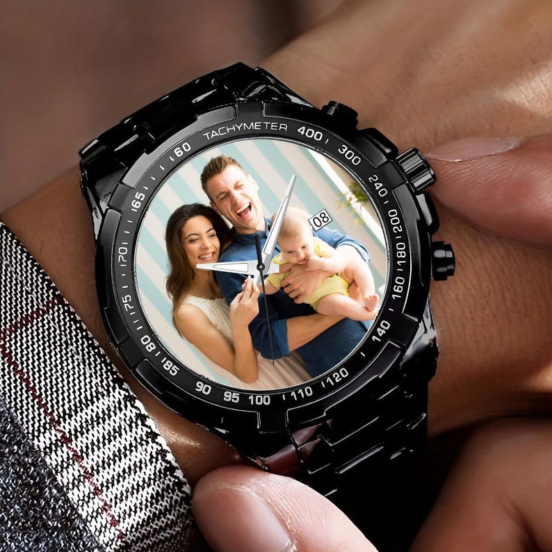 Pu&ograve; includere: Un orologio da polso nero con un quadrante bianco e una foto di una famiglia di tre persone. L'orologio ha una scala tachimetrica attorno al bordo del quadrante. La foto mostra un uomo, una donna e un bambino. L'uomo indossa una camicia blu e la donna indossa una camicia bianca. Il bambino indossa una camicia gialla. Il quadrante dell'orologio ha anche il numero 08 in alto.
