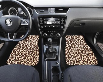 May include: Car interior with two leopard print car floor mats. The mats are tan with brown spots. The car's dashboard, steering wheel, and seats are visible. The car is parked on a road.