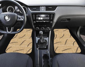 May include: Tan car floor mats with a black stitched pattern, visible inside a car's interior. The mats are placed in the driver and passenger footwells. The car's dashboard, steering wheel, and seats are also visible.