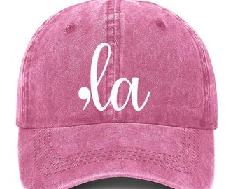 Peut inclure: Une casquette de baseball en denim rose avec le mot ".la" en lettres cursives blanches.