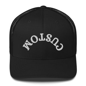 May include: Black mesh trucker hat with a white embroidered "CUSTOM" logo.