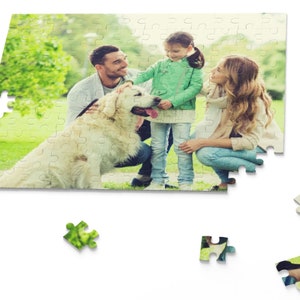 Peut inclure: Une famille avec un chien golden retriever dans un parc verdoyant. La famille est compos&eacute;e d'un homme, d'une femme et d'une jeune fille. L'homme porte une chemise bleue et un jean. La femme porte une chemise blanche et un jean. La fille porte une chemise verte et un jean. Le chien est assis sur le sol et regarde la cam&eacute;ra.