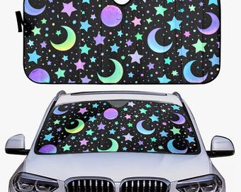 May include: Black car sunshade featuring a celestial design with colorful moons, stars, and planets. The sunshade is shown both folded and installed in a car, offering protection from the sun's rays.