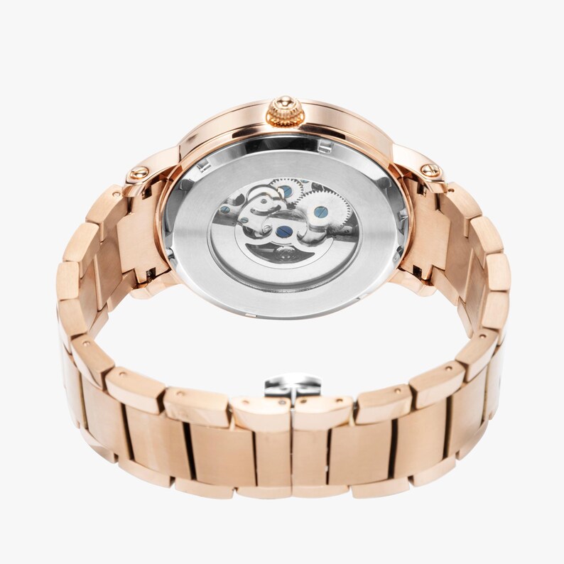 May include: Rose gold-toned wristwatch with a visible mechanical movement. The watch features a round face and a matching link bracelet. The back of the watch reveals the intricate gears and mechanisms. The watch is designed with a classic and elegant aesthetic.