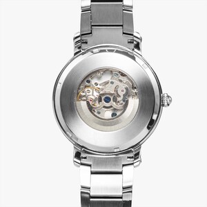 May include: A silver-toned wristwatch with a transparent back, showcasing the intricate mechanical movement. The watch features a stainless steel band and a round face, highlighting the internal gears and components.