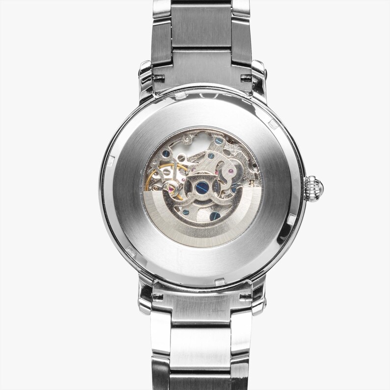May include: A silver-toned wristwatch with a transparent back, showcasing the intricate mechanical movement. The watch features a stainless steel band and a round face, highlighting the internal gears and components.