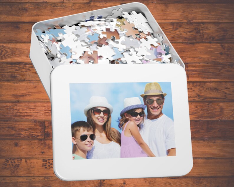 Peut inclure: Une bo&icirc;te de puzzle blanche avec une photo de famille sur le devant. La photo montre une famille de quatre personnes souriantes et portant des chapeaux. La bo&icirc;te de puzzle est ouverte et les pi&egrave;ces du puzzle sont visibles &agrave; l'int&eacute;rieur.
