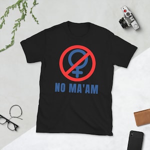 Puede incluir: Camiseta negra con un c&iacute;rculo rojo y una l&iacute;nea diagonal que atraviesa un s&iacute;mbolo femenino azul. El texto "NO MA'AM" est&aacute; impreso debajo del s&iacute;mbolo.