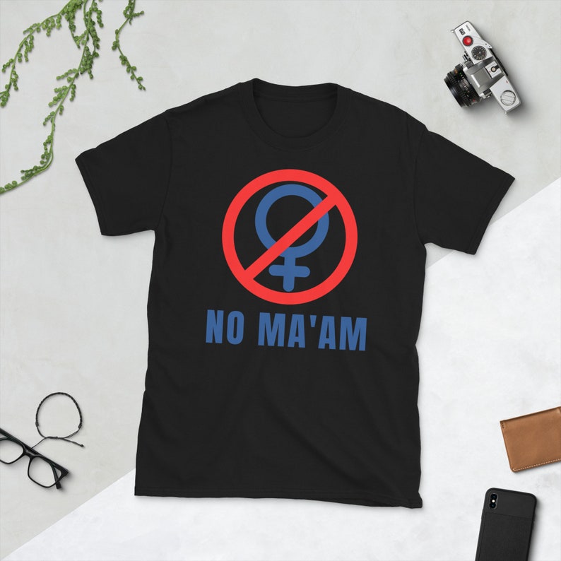 Puede incluir: Camiseta negra con un c&iacute;rculo rojo y una l&iacute;nea diagonal que atraviesa un s&iacute;mbolo femenino azul. El texto "NO MA'AM" est&aacute; impreso debajo del s&iacute;mbolo.
