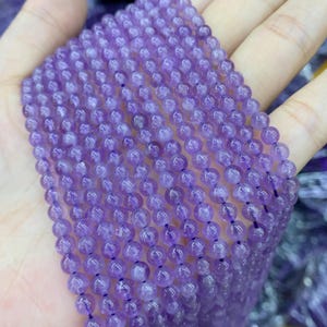 May include: A strand of polished, round amethyst beads. The beads are a deep purple color and are strung together on a dark string. The beads are smooth and have a slight sheen. The image is a close-up of the beads.