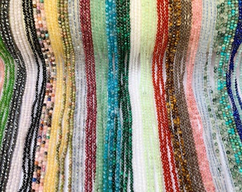 May include: A variety of gemstone beads in different colors and shapes, including black, white, green, blue, red, and brown. The beads are strung on a white background.