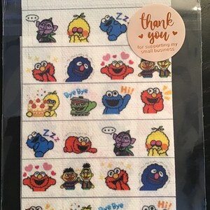 May include: A sheet of stickers featuring Sesame Street characters in various poses. The stickers are arranged in horizontal rows and include Elmo, Cookie Monster, Big Bird, and others. A round sticker with the text "thank you" is on the packaging.