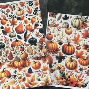 May include: Two sheets of decorative paper with a repeating pattern of pumpkins, leaves, and berries in shades of orange, brown, and green on a white background. The design evokes a fall or harvest theme.