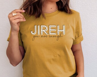 Può includere: Una maglietta color senape con il testo "JIREH you are enough" in lettere bianche e marroni.