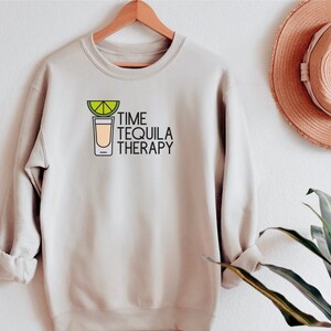 Może przedstawiać: Jasnobeżowa bluza z nadrukiem kieliszka do shotów z plasterkiem limonki i tekstem "TIME TEQUILA THERAPY".