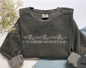 Puede incluir: Una sudadera gris oscuro con un gráfico blanco de olas y el texto "Si los océanos rugen tu grandeza, yo también lo haré".