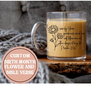 May include: A clear glass mug with a black outline of a daisy and the text "surely Your goodness and love will follow me all the days of my life Psalm 236".