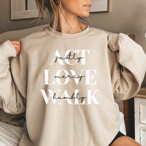 Może przedstawiać: Beżowa bluza z nadrukiem "ACT justly LOVE mercy WALK humbly" w kolorze białym na przodzie.
