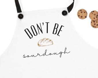 May include: White apron with black straps and buttons. The apron has a black graphic that says "Don't be sourdough" with a drawing of a loaf of bread.