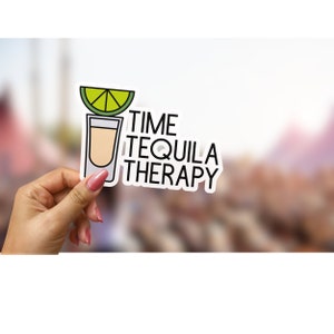 May include: White sticker with a black outline and the text "TIME TEQUILA THERAPY". A cartoon image of a shot glass with a lime wedge on top is to the left of the text.