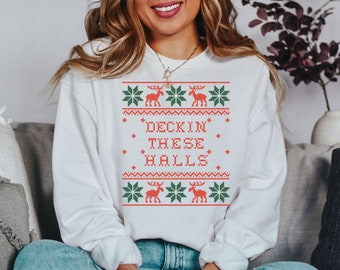 May include: White Christmas sweater with a red and green design featuring reindeer and snowflakes. The sweater has the text "Deck'n These Halls" in red.