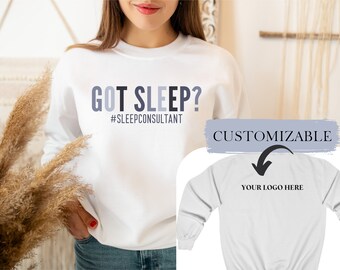 May include: White sweatshirt with the text "GOT SLEEP? #SLEEPCONSULTANT" printed on the front. The back of the sweatshirt is blank with the text "CUSTOMIZABLE" and an arrow pointing down to the text "YOUR LOGO HERE".