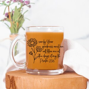 May include: A clear glass mug with a black outline of flowers and the text "surely Your goodness and love will follow me all the days of my life Psalm 236".