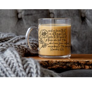 May include: A clear glass mug with a black floral design and the text "and we know that in all things God works for the good of Those who love Him who have been called according to His purpose Romans 828".