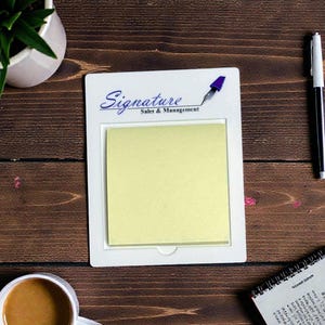 Può includere: Un portablocco bianco con un post-it giallo, le parole "Signature Sales & Management" sono stampate in alto. Una penna bianca e nera e una tazza di caffè sono accanto al portablocco. Una piccola pianta in un vaso bianco si trova nell'angolo in alto a sinistra.