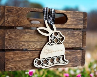 Op de afbeelding: Een houten paaseierenhanger in de vorm van een konijn met een geometrisch patroon en de naam "Stephanie" erop gegraveerd. De hanger hangt aan een zwart-wit geblokt lint.
