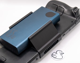 May include: A black Nintendo Switch console with a blue power bank attached to it using a black charging stand. The power bank has the text "52W" printed on it.