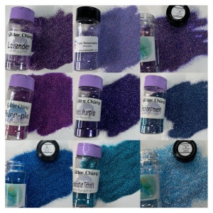 May include: Assortment of small jars filled with various colors of glitter. The jars are labeled with the name "Glitter Chimp" and the color of the glitter. The colors include lavender, purple, crystal purple, enchantment, and teal.