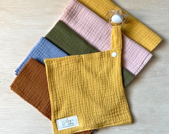 Peut inclure: Un ensemble de six langes en mousseline pour bébé de 20,3 x 20,3 cm dans différentes couleurs, dont le jaune moutarde, le marron, le vert, le bleu et le rose. Les langes ont une fermeture à pression et une boucle pour attacher une sucette. Les langes sont fabriqués par Lucy's Little Shop.