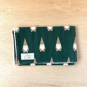 May include: A green burp cloth with a white border and a repeating pattern of brown gnomes. The cloth has a white label with the text "Lucy's Little" on it.