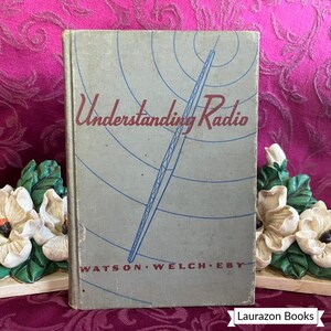 May include: A vintage book titled "Understanding Radio" with a light blue cover. The cover features a blue antenna illustration and the names WATSON WELCH EBY. The book is displayed on a decorative surface.