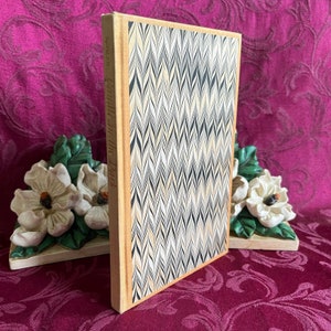 May include: A book titled "Candles in the Dark" with a marbled cover featuring a chevron pattern in black, white, and gold.