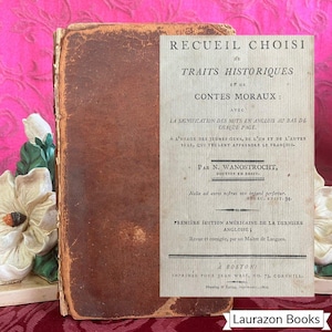 May include: Antique book with a worn, brown leather cover and a cream-colored title page. The title reads "RECUEIL CHOISI DE TRAITS HISTORIQUES ET DE CONTES MORAUX." Text in French and English is visible. The book is from Boston.