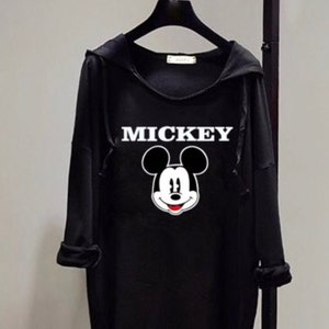 Puede incluir: Sudadera con capucha negra con un gr&aacute;fico de Mickey Mouse blanco y la palabra "MICKEY" impresa en blanco.