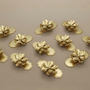 May include: Gold-colored cabinet pulls with a floral design. Each pull features a flower-shaped handle mounted on a rectangular backplate. The hardware is arranged on a neutral background, showcasing the decorative details.