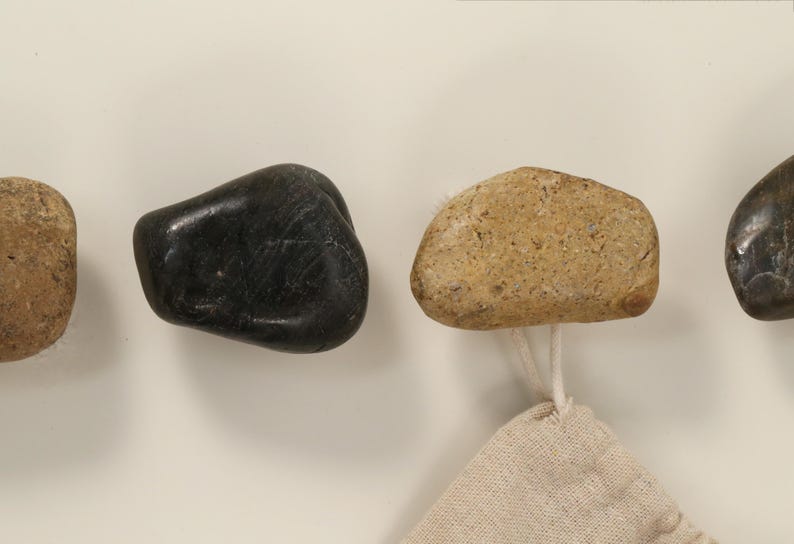 May include: A collection of natural stone hooks in various colors, including black and tan. Each hook is attached to a small, beige fabric loop, suitable for hanging items. The hooks are mounted on a white surface.