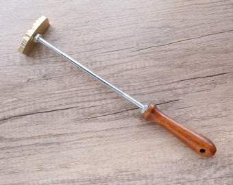 May include: A metal and wood tool with a textured, scalloped head and a wooden handle. The tool is used for pressing designs into dough.