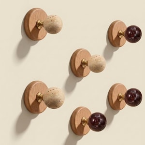 May include: A selection of wall-mounted coat hooks. Each hook has a circular wooden base with a brass fitting, supporting either a light-colored stone sphere or a dark red, marbled ball. The hooks are displayed against a plain background.