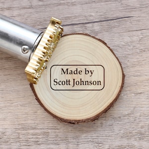 以下が含まれることがあります： 木製の丸い板に「Made by Scott Johnson」という文字が刻まれた金色の金属製のスタンプ