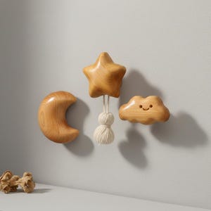 Puede incluir: Juego de decoración de pared de madera con una luna creciente, una estrella de cinco puntas con borla y una nube sonriente. El conjunto está hecho de madera clara y está diseñado para una guardería o habitación infantil. La nube tiene una cara sonriente tallada.