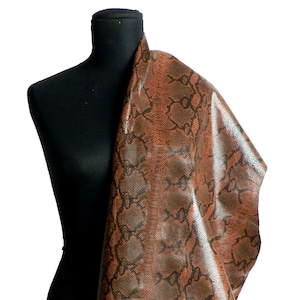Peut inclure: Un tissu en peau de serpent brun avec un motif noir. Le tissu est drapé sur un mannequin noir.