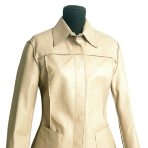 Può includere: Una giacca di pelle color crema con chiusura a bottoni, maniche lunghe e due tasche sul davanti.