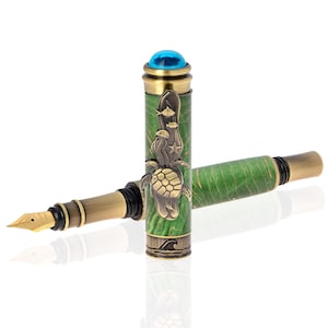 May include: A fountain pen with a green and gold barrel, featuring a sea turtle and fish design. The pen has a gold nib and a blue gem on the cap. The pen is a writing instrument.