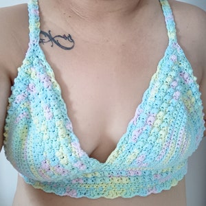 May include: A pastel-colored crochet top in shades of blue, yellow, and pink. The top features a halter-style design with a scalloped edge along the bottom. The handmade garment is a soft, textured piece.