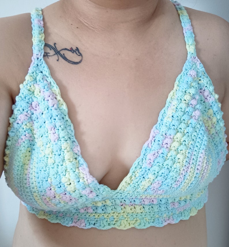 May include: A pastel-colored crochet top in shades of blue, yellow, and pink. The top features a halter-style design with a scalloped edge along the bottom. The handmade garment is a soft, textured piece.